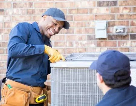 Two technicians working on an outdoor residential air conditioning unit