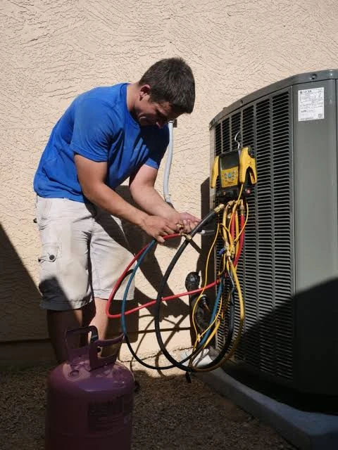 HVAC technician checking gauges and refrigerant lines at an outdoor condenser
