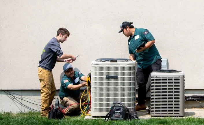 Three technicians inspecting residential outdoor heating and cooling equipment