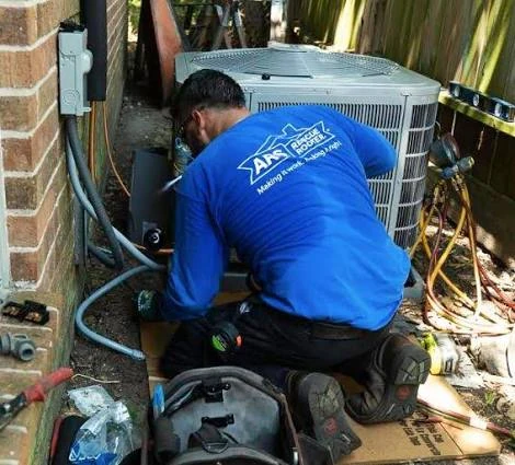 Technician kneeling beside an outdoor condenser to inspect its connections
